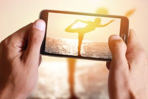 Male hand taking photo of Silhouette of young woman practicing yoga on the beach near the sea, ocean at sunset with cell, mobile phone.